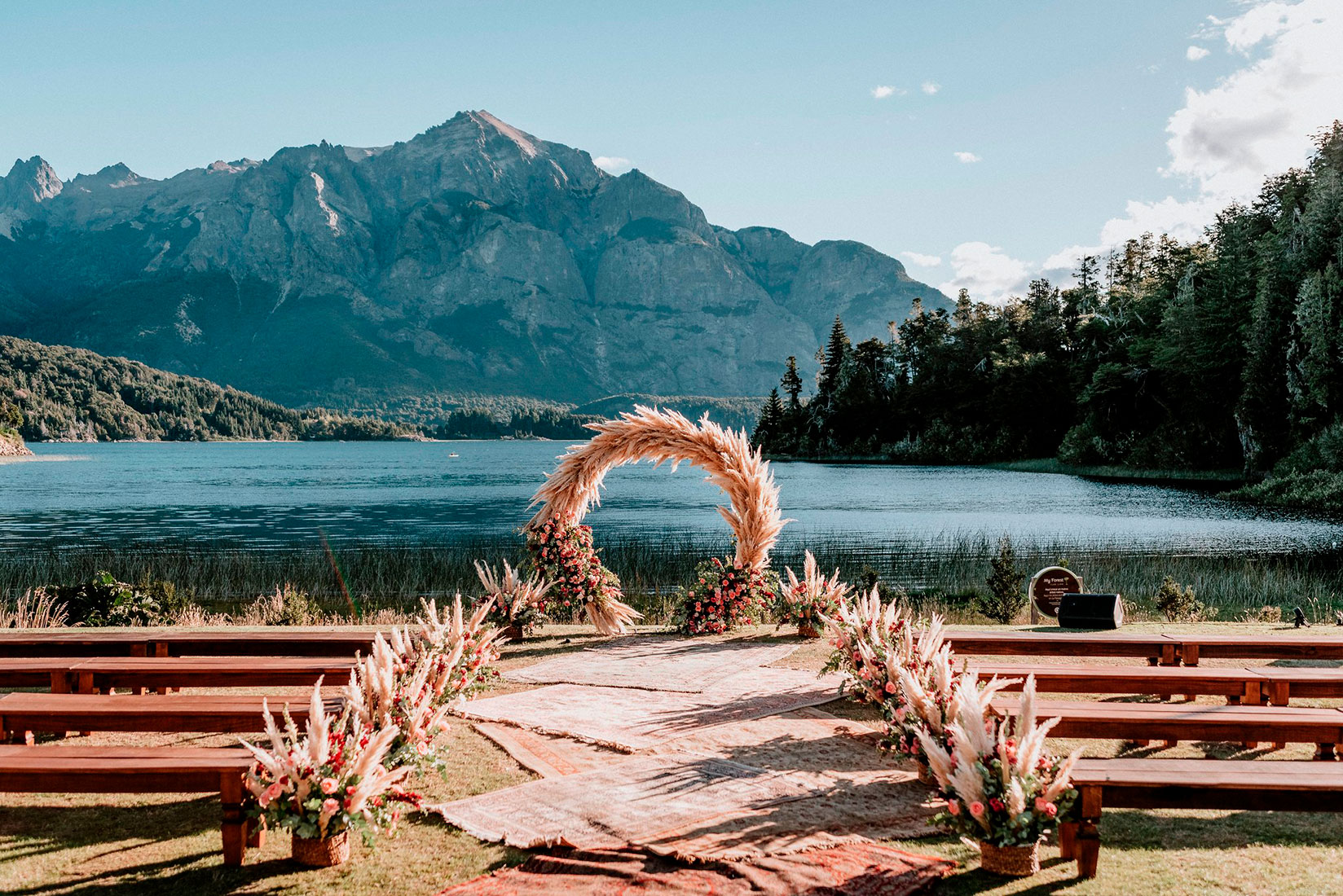 Bellísimo altar frente al lago Nahuel Huapi, detrás un fondo majestuoso de montañas y vegetación del extraordinario destino de bodas, Bariloche. Organizado por Dupla Planners.