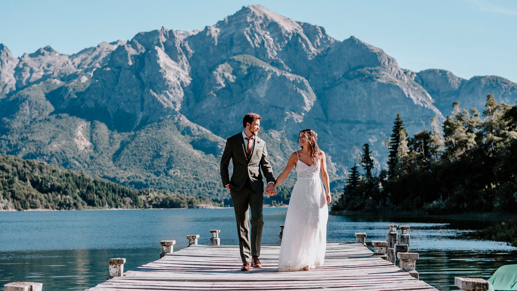 Angie & David caminan de la mano por el muelle lago Nahuel Huapi celebracion boda Patagonia argentina Dupla Planners Destination Wedding