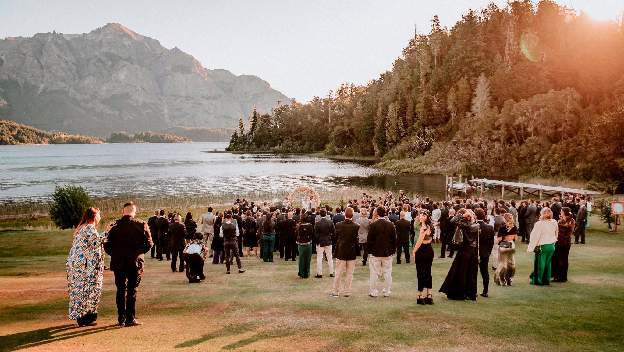 Altar frente al lago Nahuel Huapi y las majestuosas montañas de fondo coronan la celebración de la boda. Junto a los novios están muchos invitados disfrutando de la mágica experiencia organizada por Dupla Planners.