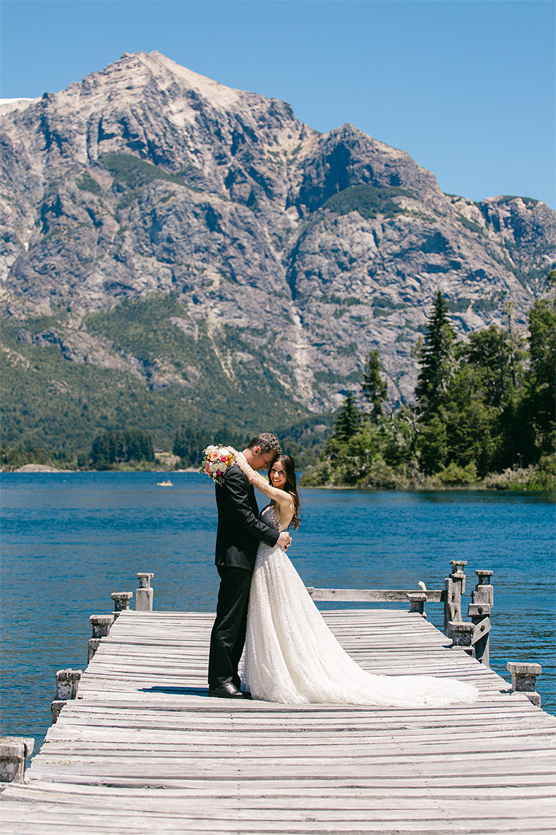 Los novios en el muelle del lago Nahuel Huapi disfrutan de la intimidad de un abrazo rodeados de la bellísima naturaleza de Patagonia. Dupla Planners lo hizo posible.