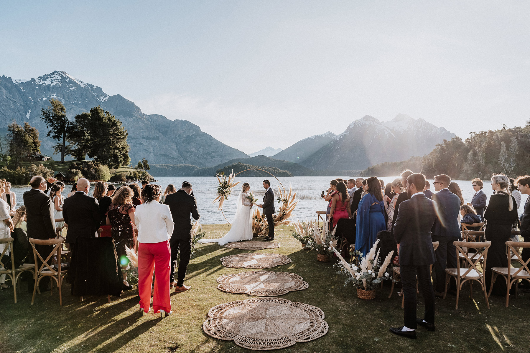 Los novios frente al altar junto a sus seres queridos celebrando su boda en un extraordinario escenario de montañas y lago en Bariloche, Patagonia, Argentina. Dupla Planners lo hizo posible.